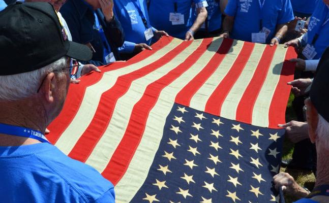 A group of people in blue shirts unfurl an American flag.